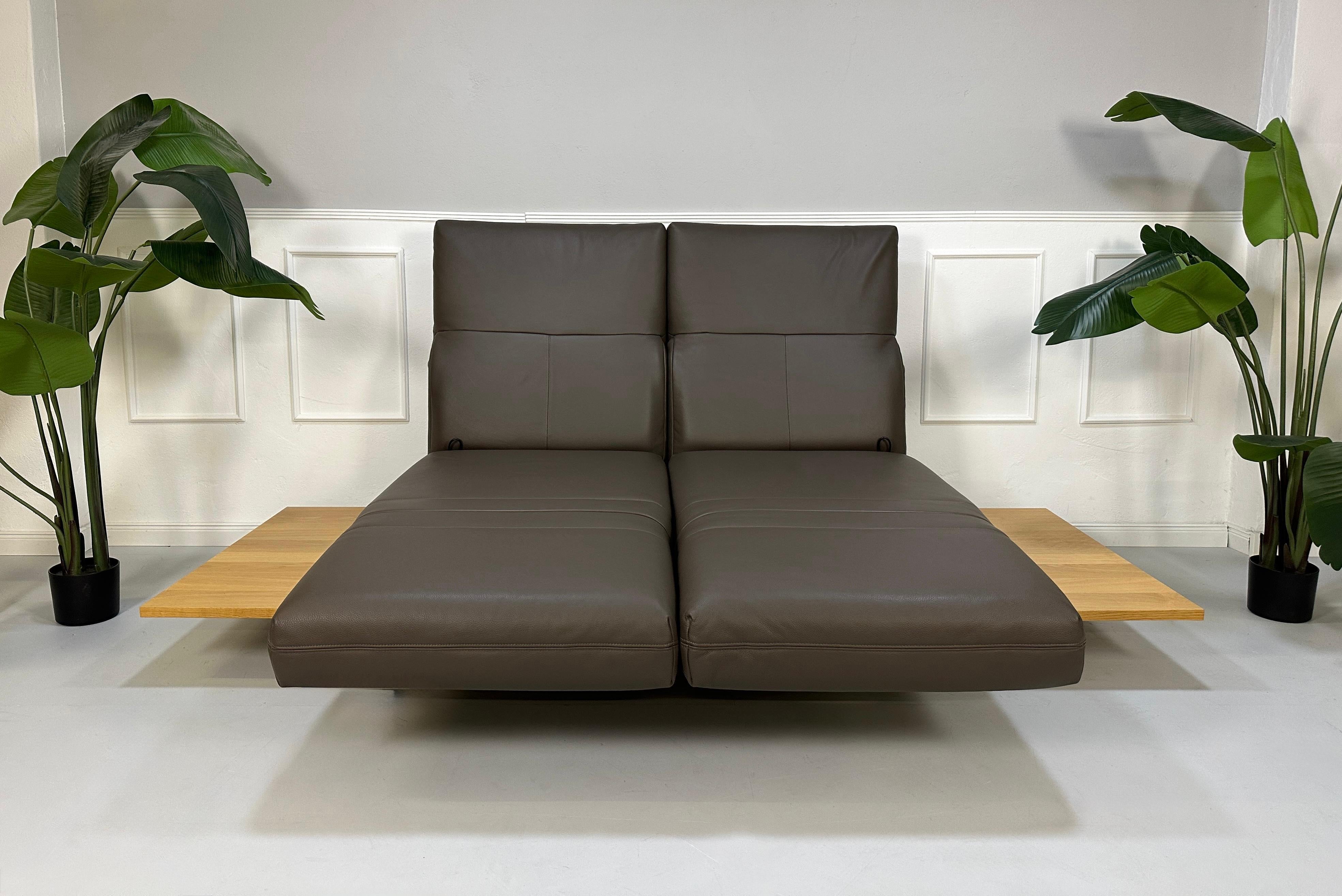 Gebrauchtes braunes Rolf Benz Aura Designer Leder Sofa vor einer Wand, stilvoll und modern eingerichtet.