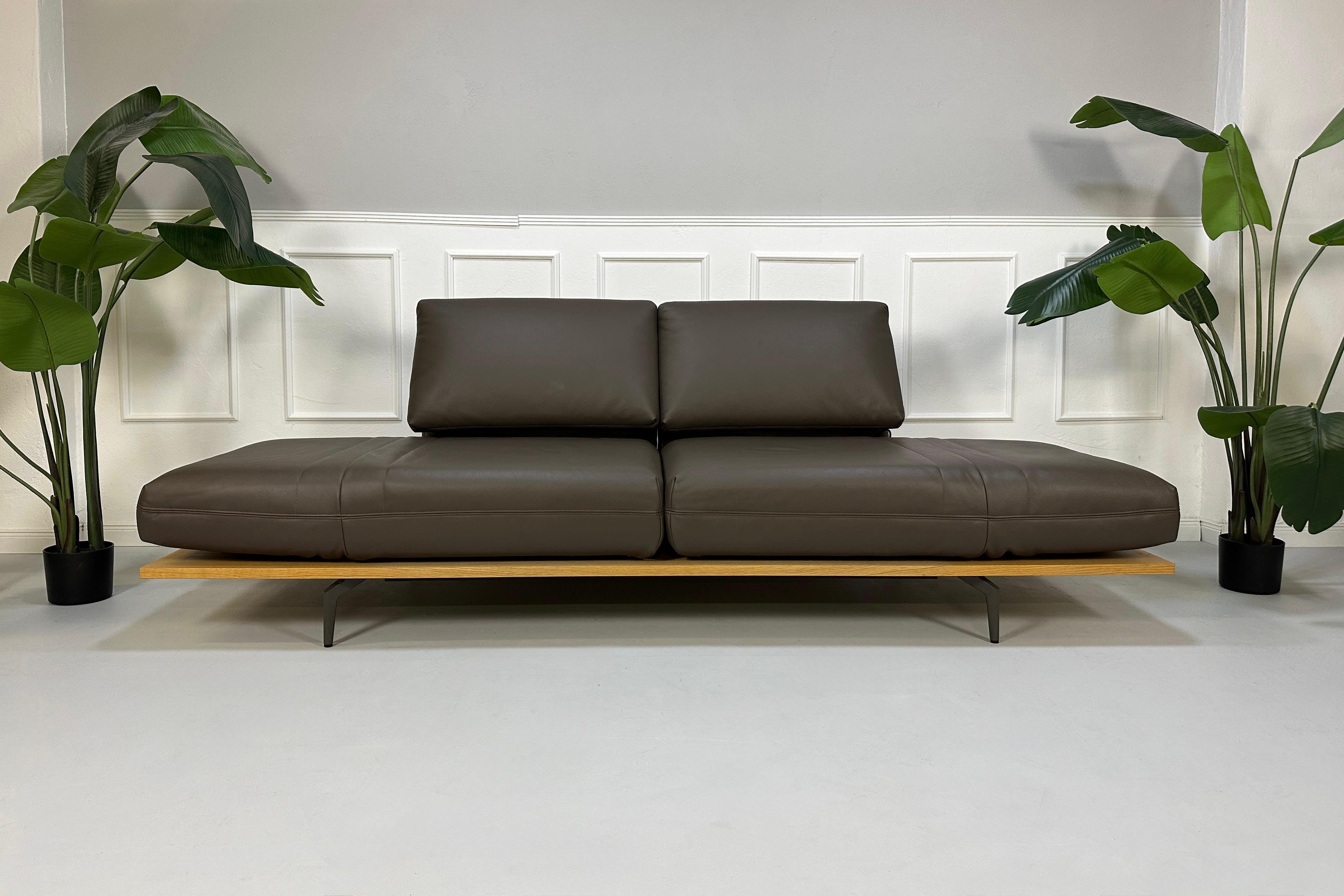 Gebrauchtes braunes Rolf Benz Aura Designer Leder Sofa vor einer Wand, stilvoll und modern eingerichtet.