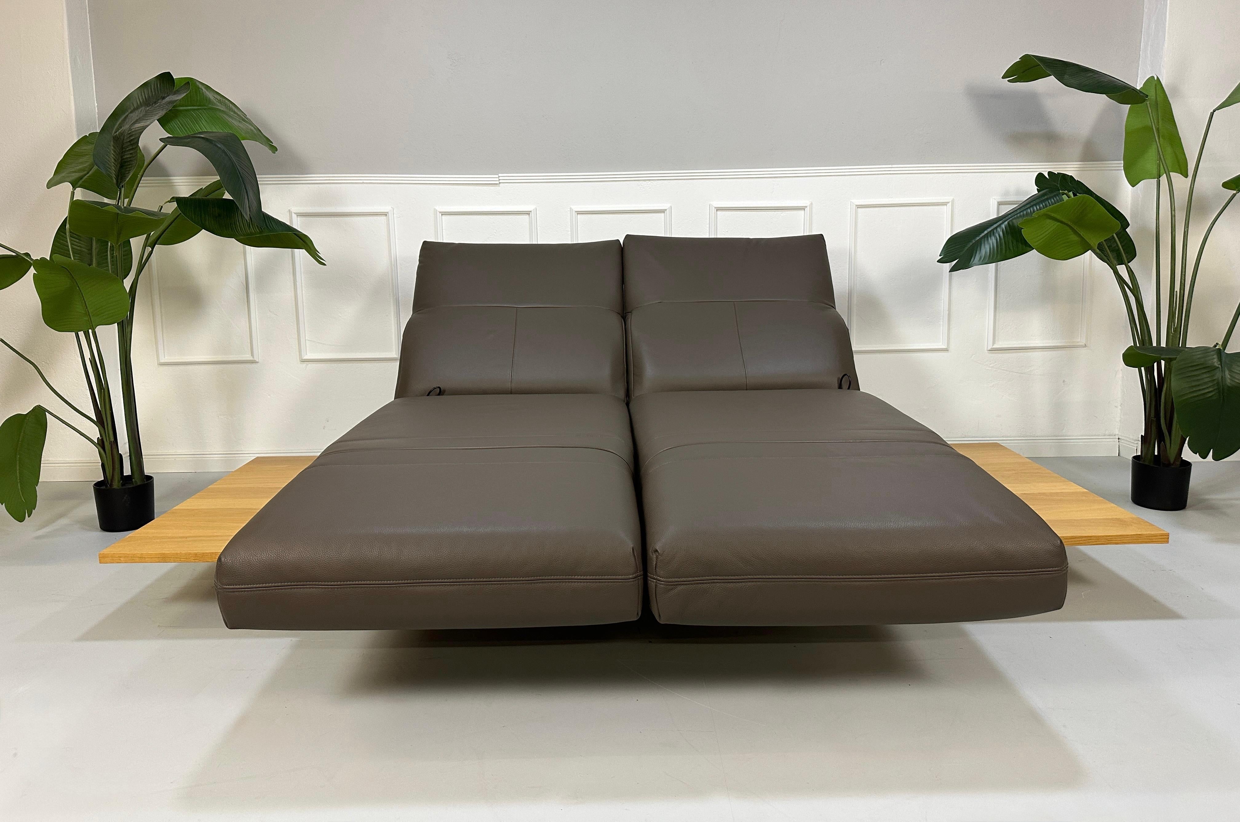 Gebrauchtes braunes Rolf Benz Aura Designer Leder Sofa vor einer Wand, stilvoll und modern eingerichtet.