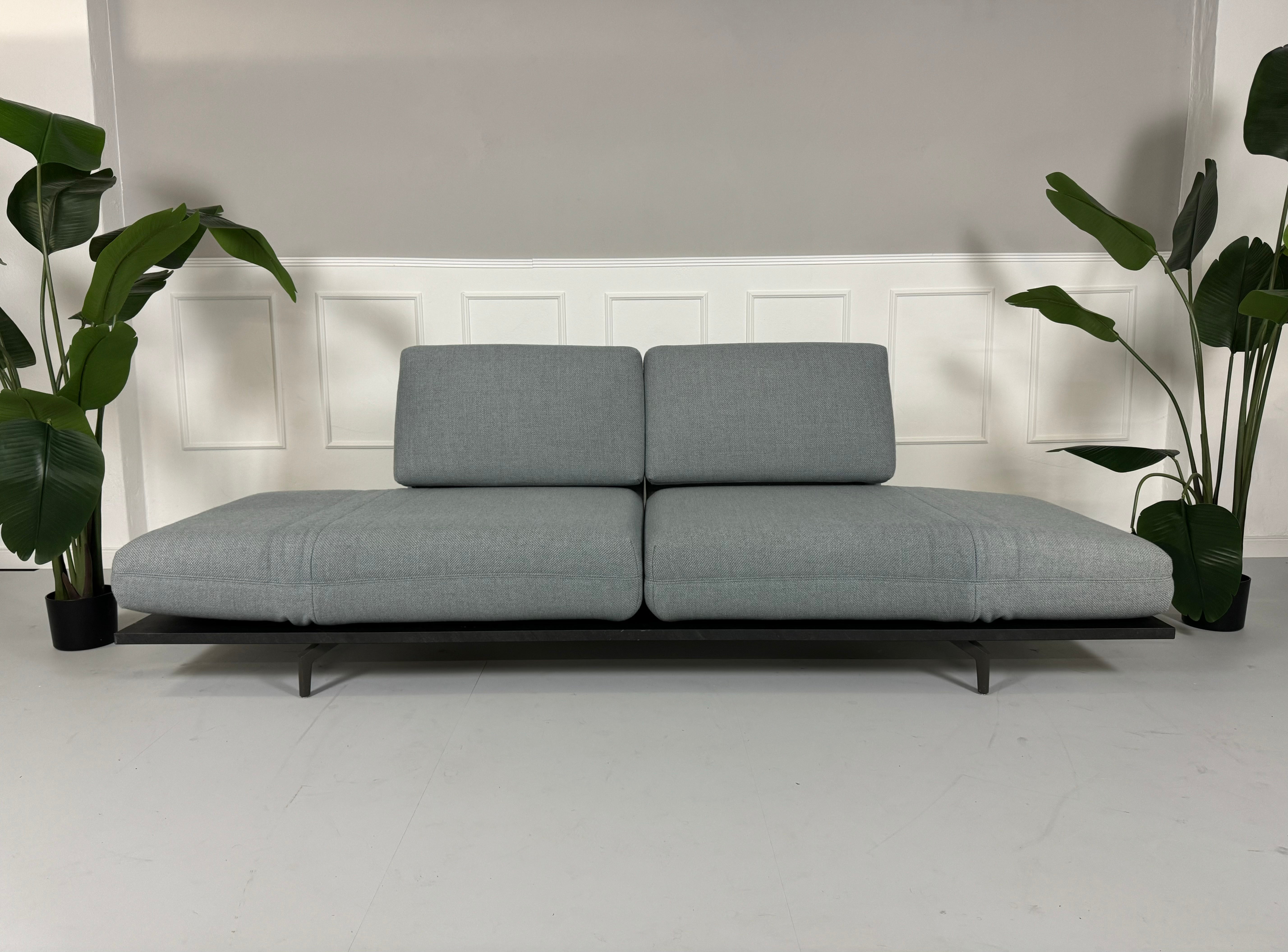 Gebrauchtes blaues Rolf Benz Aura 388 Designer Stoff Sofa vor einer Wand, stilvoll und modern eingerichtet.