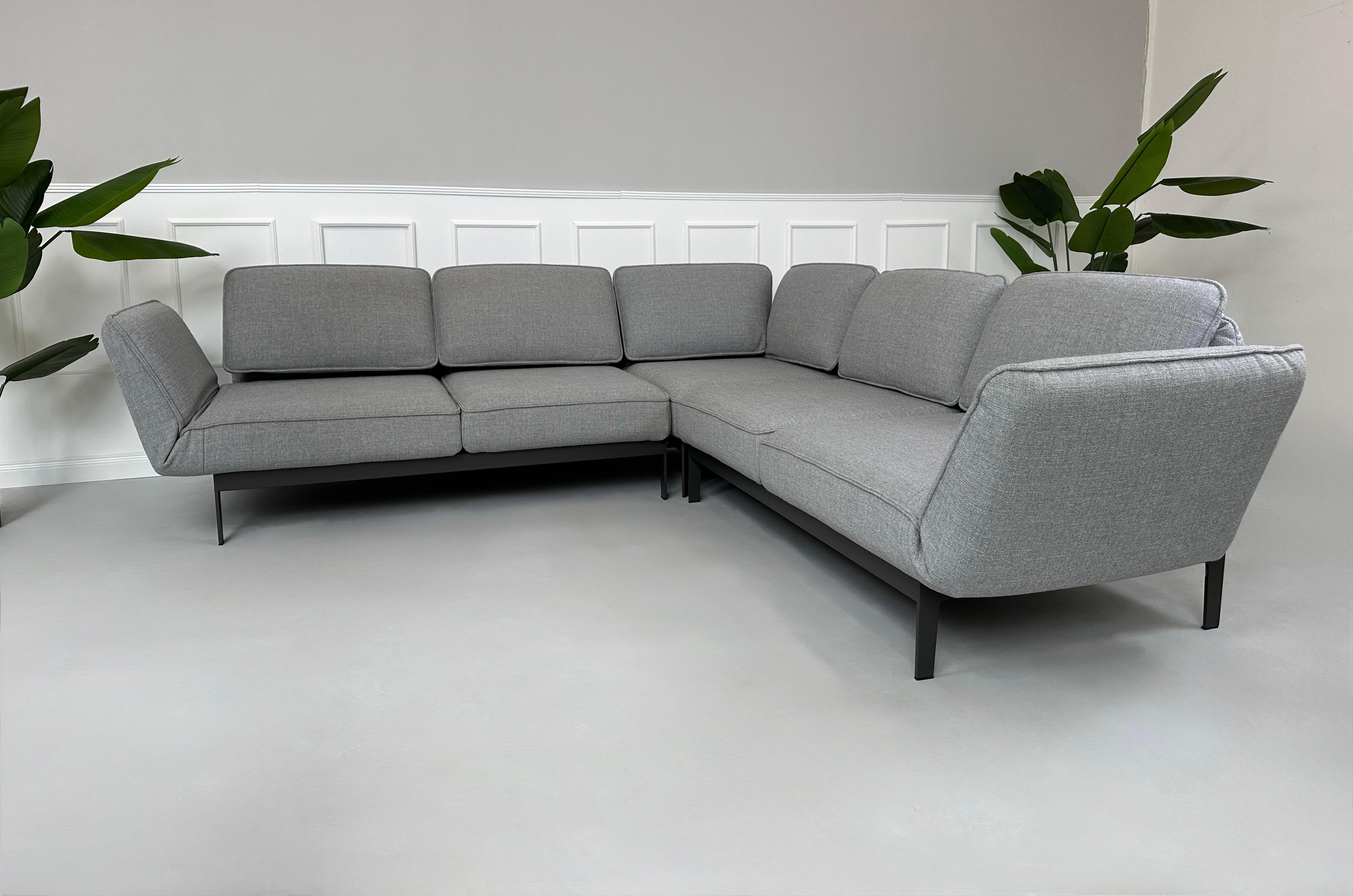 Graues Ausstellungsstück Rolf Benz Mera Designer Stoff Sofa vor einer Wand, stilvoll und modern eingerichtet.