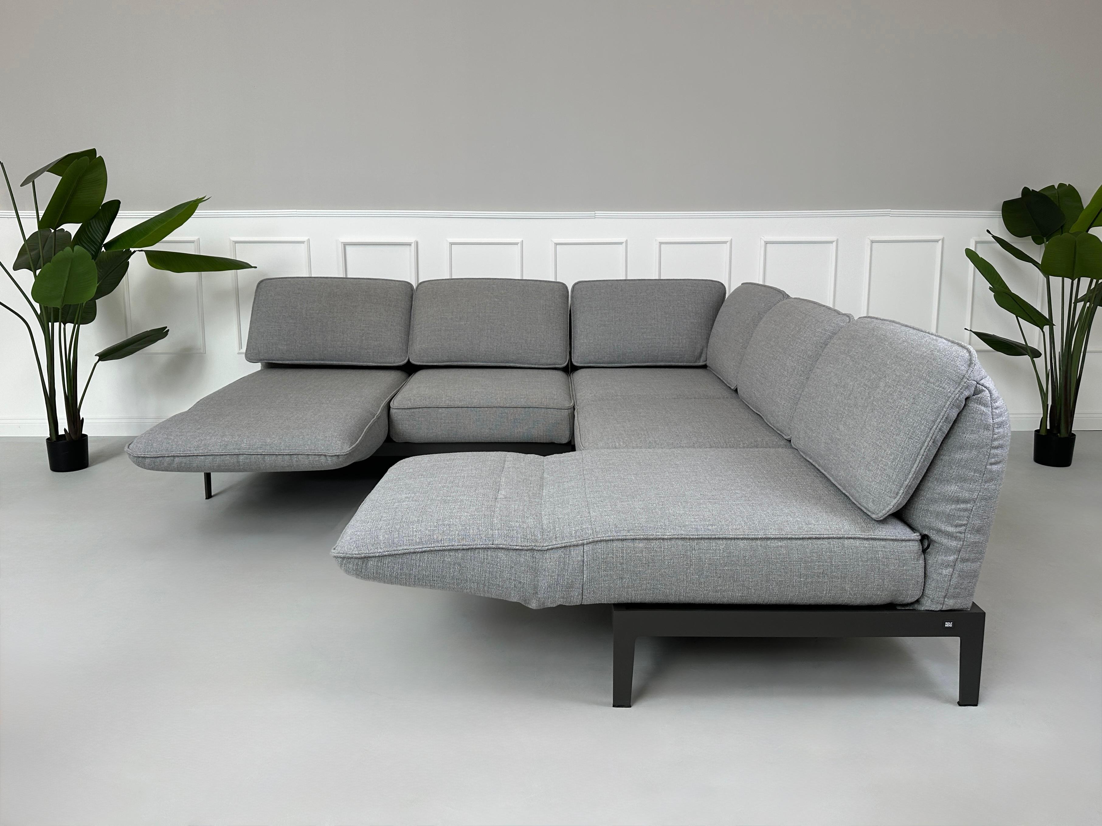 Graues Ausstellungsstück Rolf Benz Mera Designer Stoff Sofa vor einer Wand, stilvoll und modern eingerichtet.