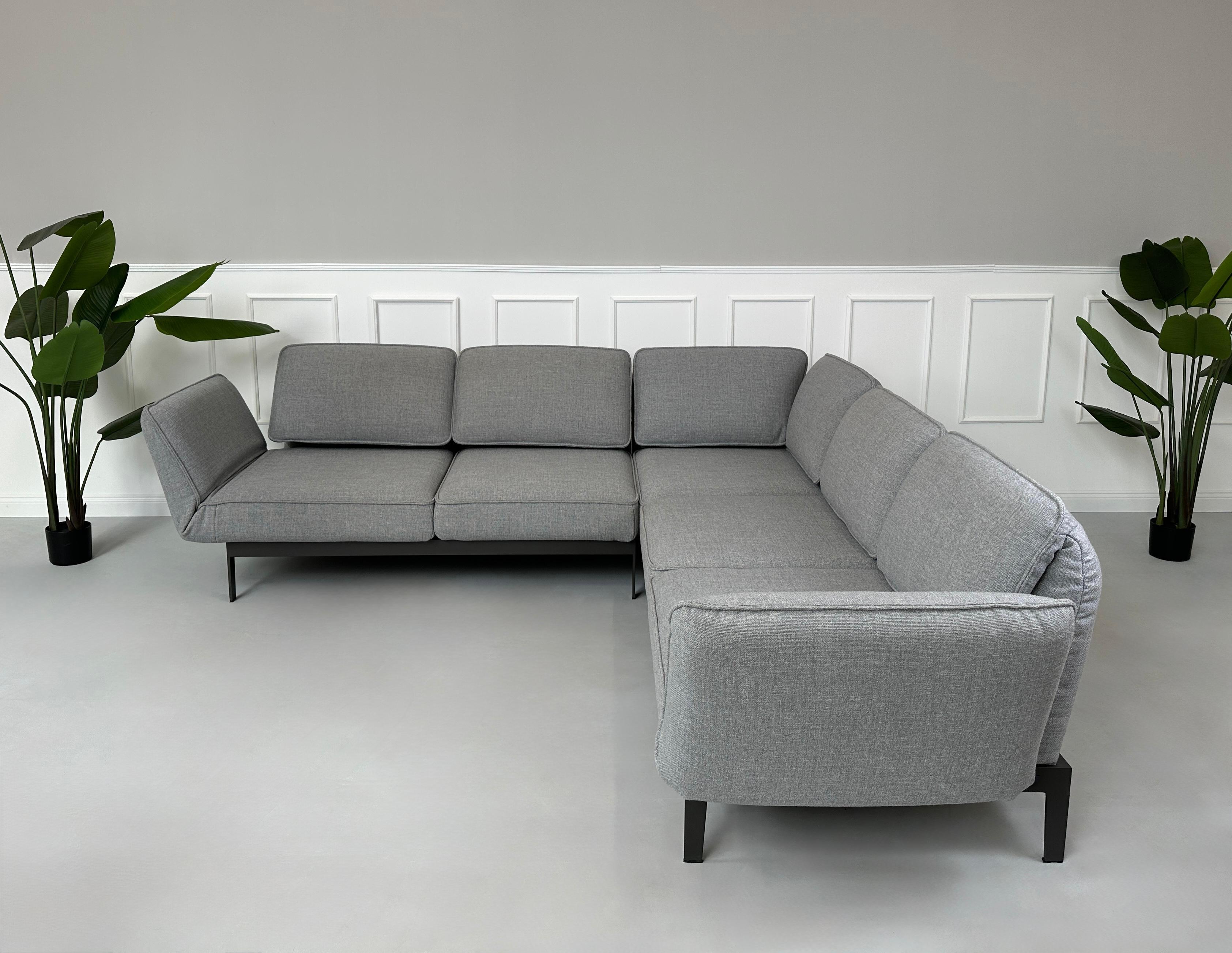 Graues Ausstellungsstück Rolf Benz Mera Designer Stoff Sofa vor einer Wand, stilvoll und modern eingerichtet.