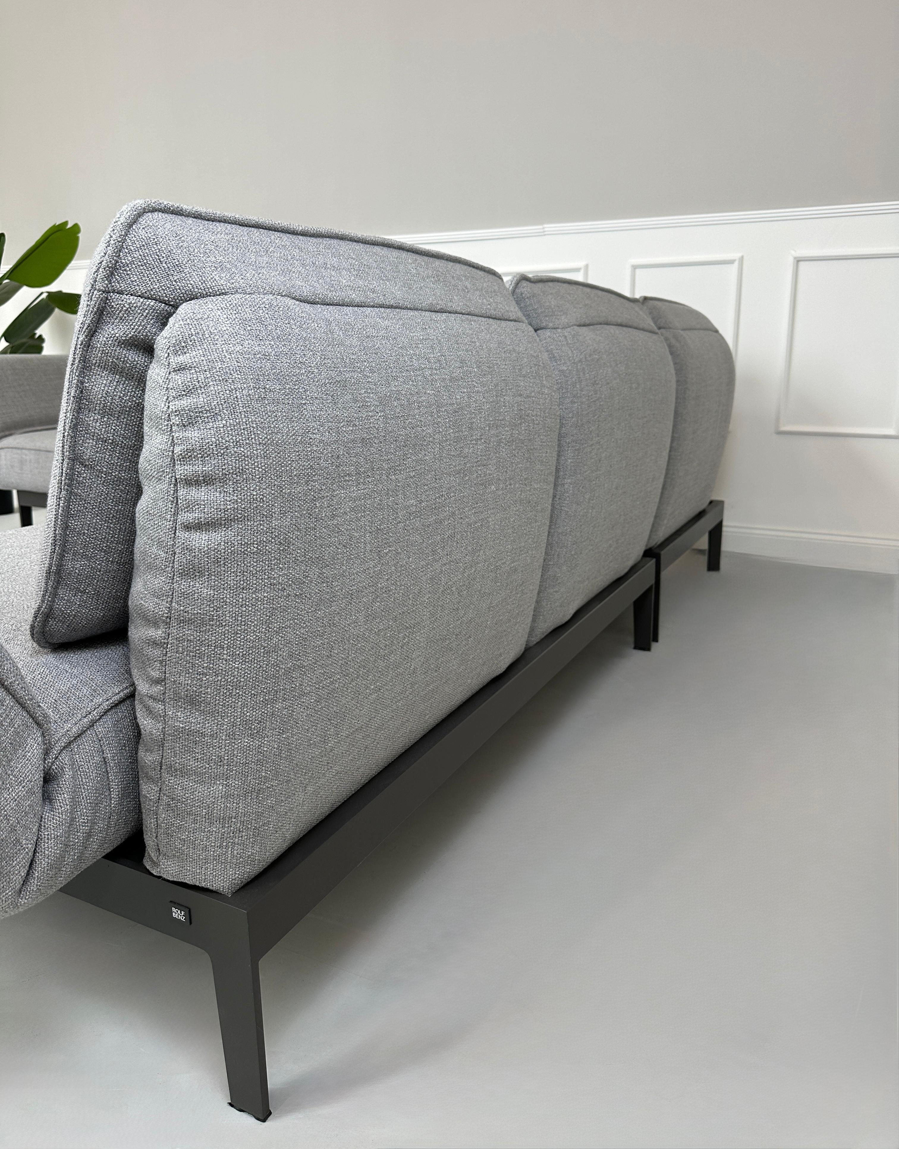 Graues Ausstellungsstück Rolf Benz Mera Designer Stoff Sofa vor einer Wand, stilvoll und modern eingerichtet.