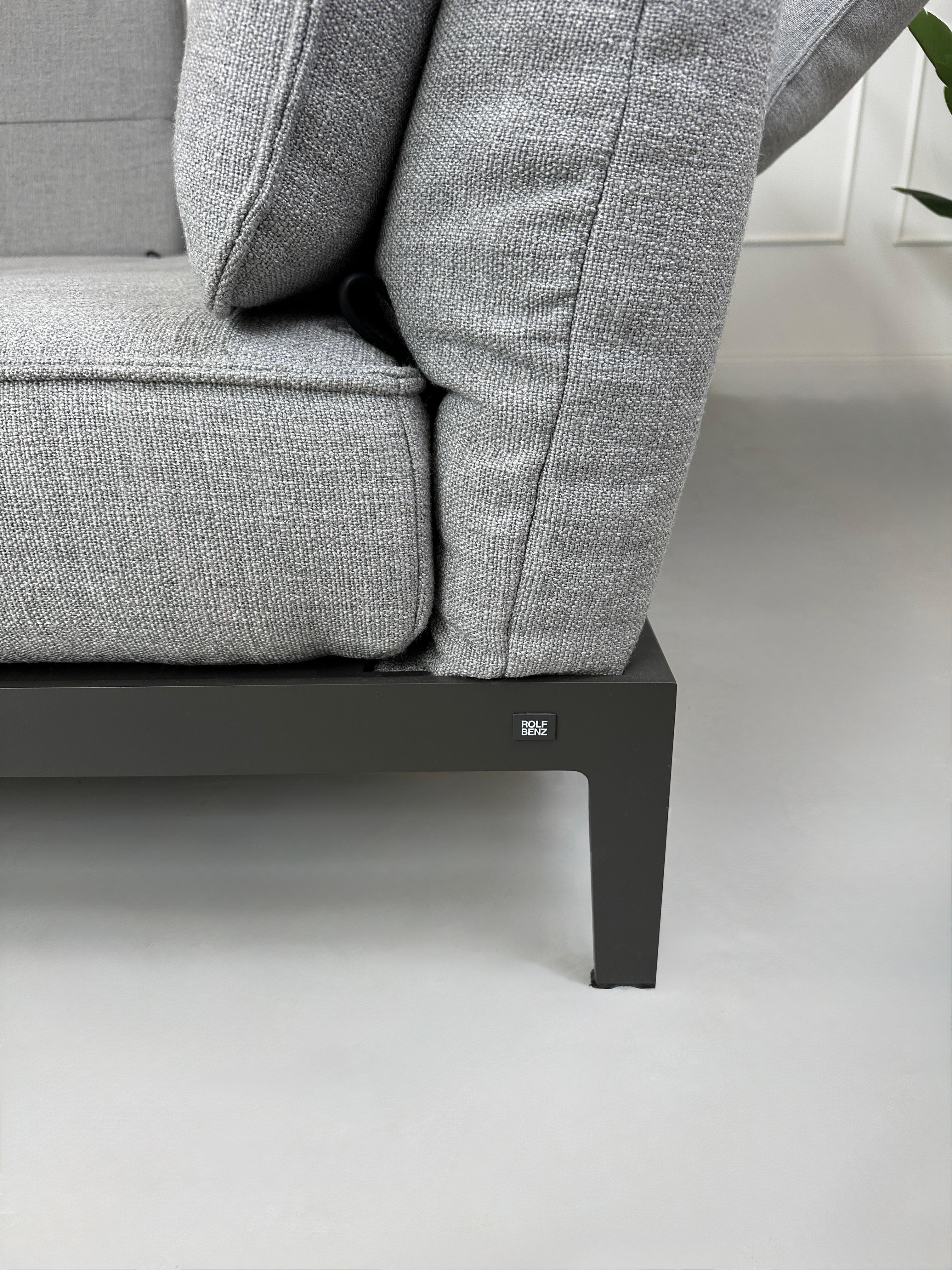 Graues Ausstellungsstück Rolf Benz Mera Designer Stoff Sofa vor einer Wand, stilvoll und modern eingerichtet.