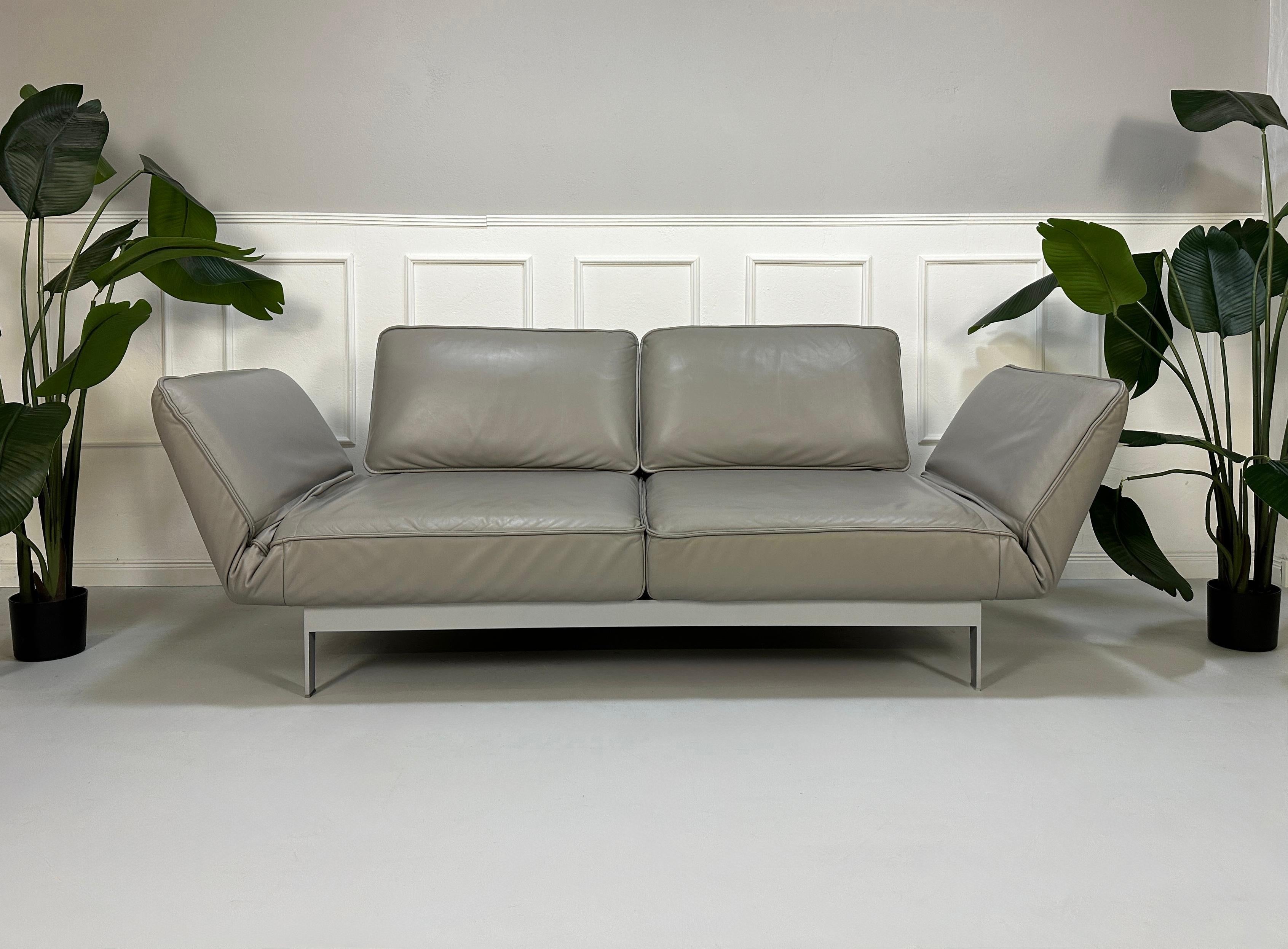 Gebrauchtes graues Rolf Benz Designer Leder Sofa vor einer Wand, stilvoll und modern eingerichtet.