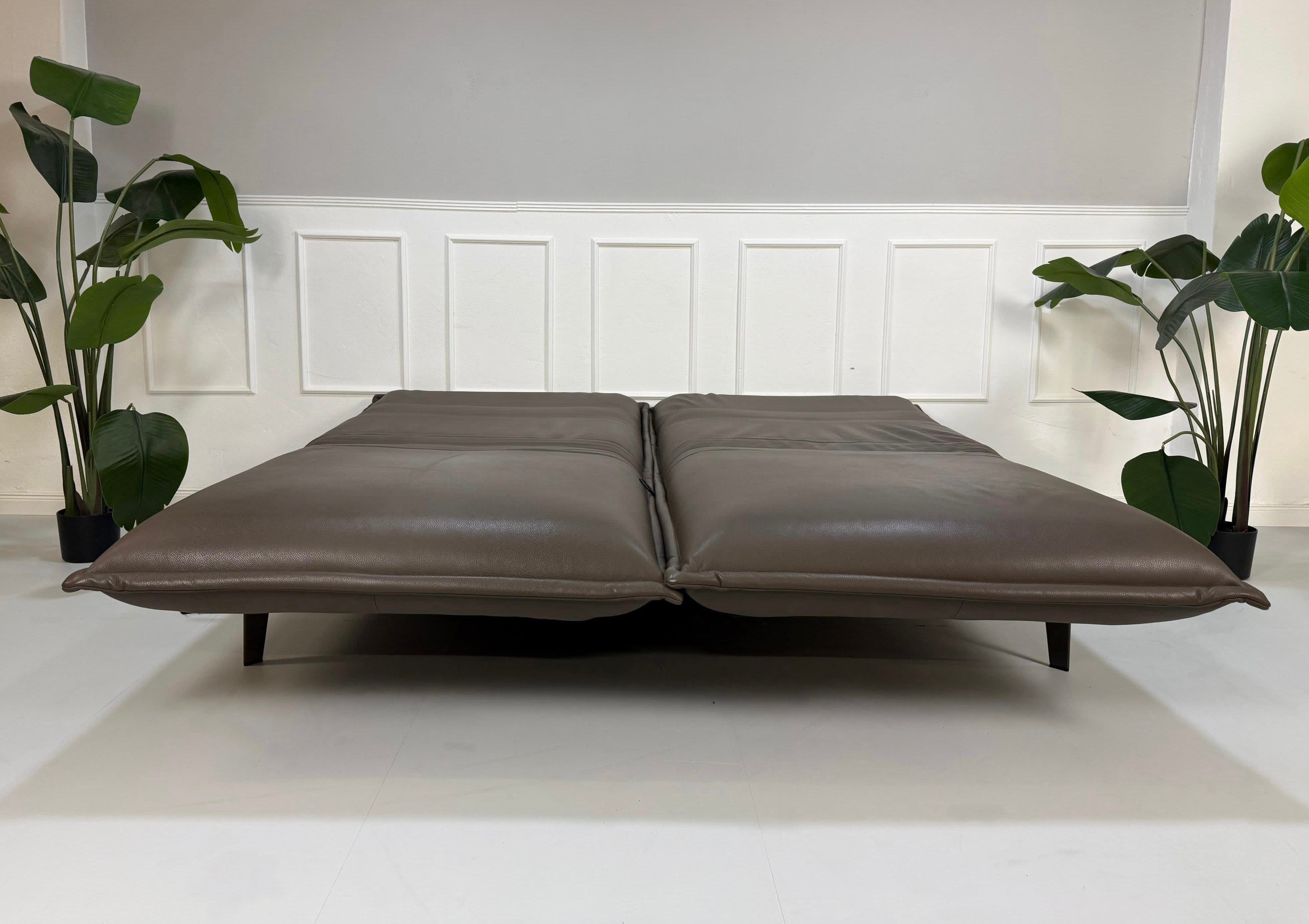 Gebrauchtes braunes Rolf Benz Designer Leder Sofa vor einer Wand, stilvoll und modern eingerichtet.