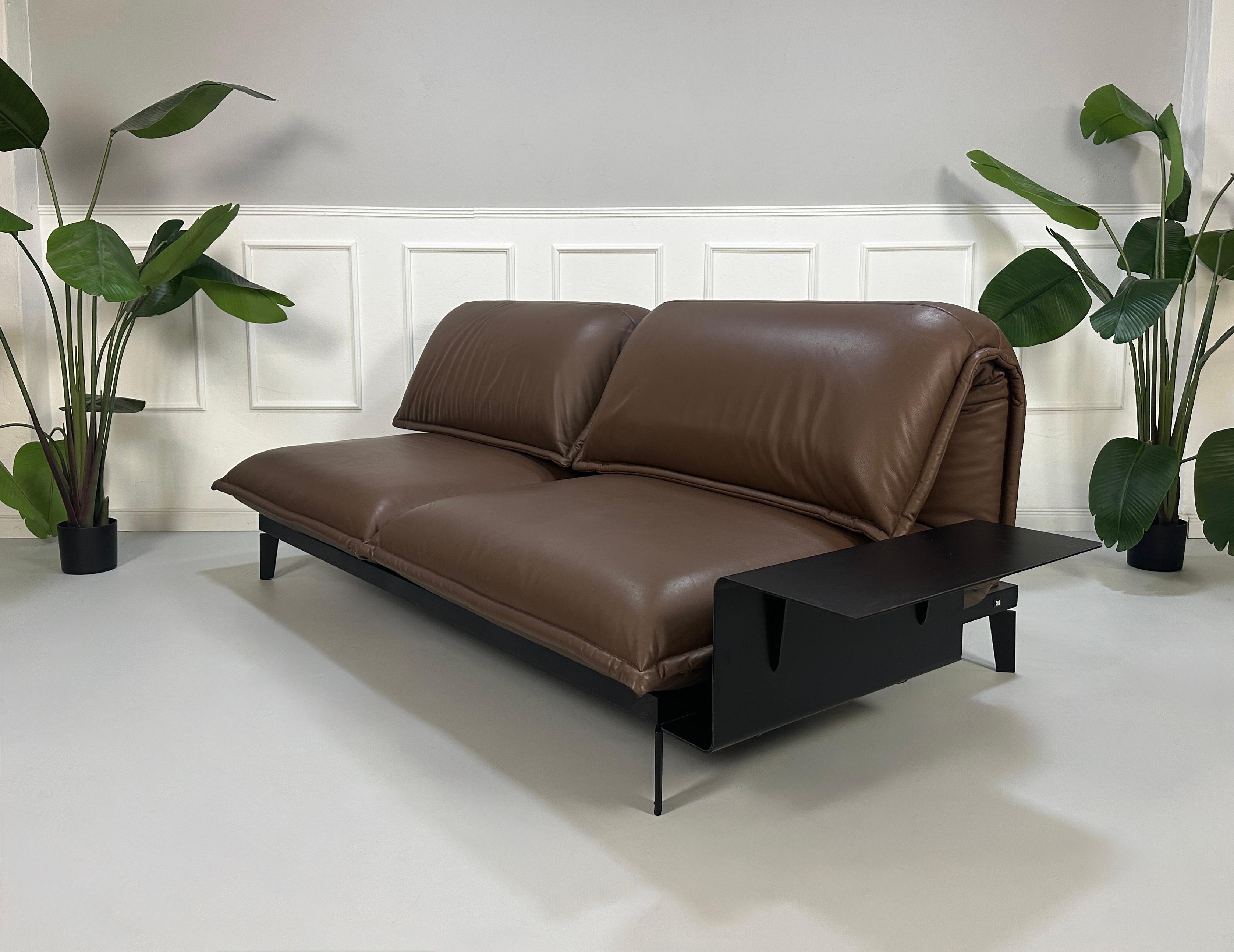 Gebrauchtes braunes Rolf Benz Nova Designer Leder Sofa vor einer Wand, stilvoll und modern eingerichtet.