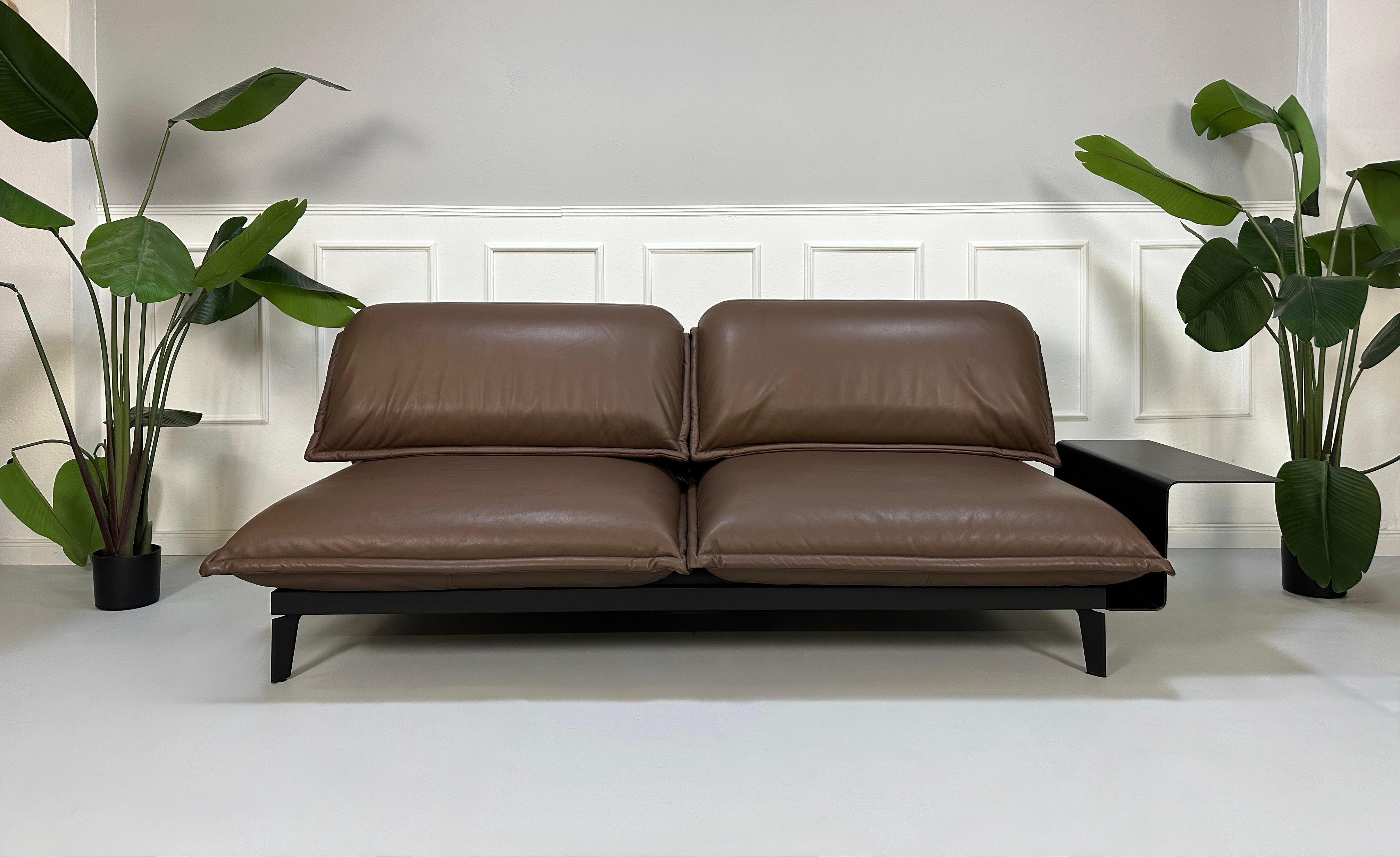 Gebrauchtes braunes Rolf Benz Nova Designer Leder Sofa vor einer Wand, stilvoll und modern eingerichtet.