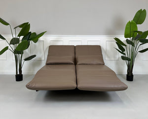 Gebrauchtes braunes Rolf Benz Plura Designer Leder Sofa mit Hocker vor einer Wand, stilvoll und modern eingerichtet.