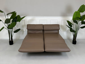 Gebrauchtes braunes Rolf Benz Plura Designer Leder Sofa mit Hocker vor einer Wand, stilvoll und modern eingerichtet.