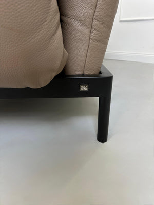 Gebrauchtes braunes Rolf Benz Plura Designer Leder Sofa mit Hocker vor einer Wand, stilvoll und modern eingerichtet.