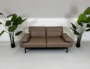 Gebrauchtes braunes Rolf Benz Plura Designer Leder Sofa mit Hocker vor einer Wand, stilvoll und modern eingerichtet.