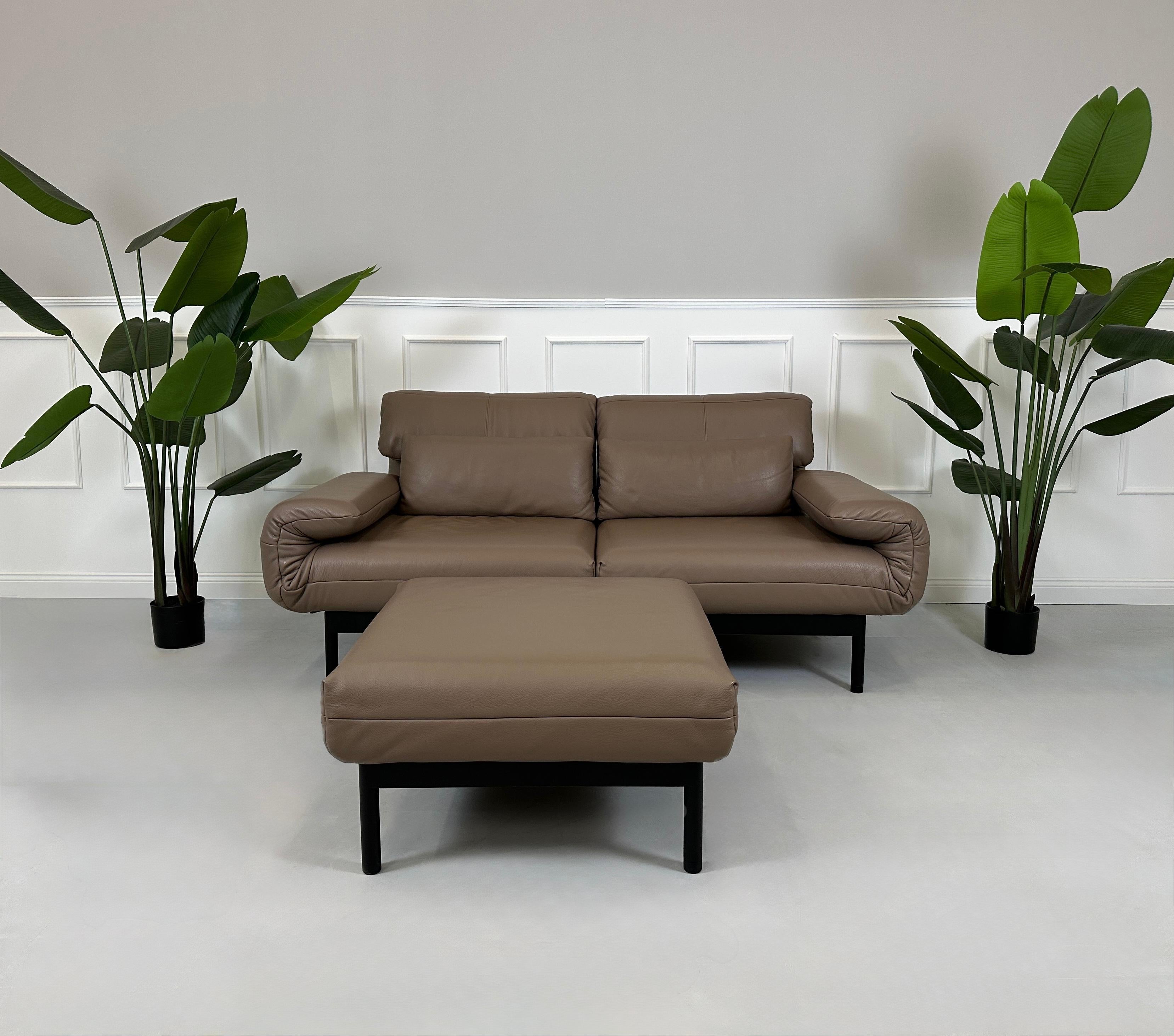 Gebrauchtes braunes Rolf Benz Plura Designer Leder Sofa mit Hocker vor einer Wand, stilvoll und modern eingerichtet.