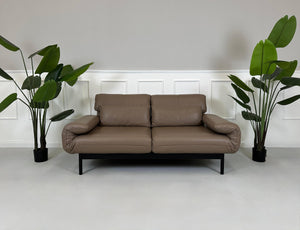 Gebrauchtes braunes Rolf Benz Plura Designer Leder Sofa mit Hocker vor einer Wand, stilvoll und modern eingerichtet.