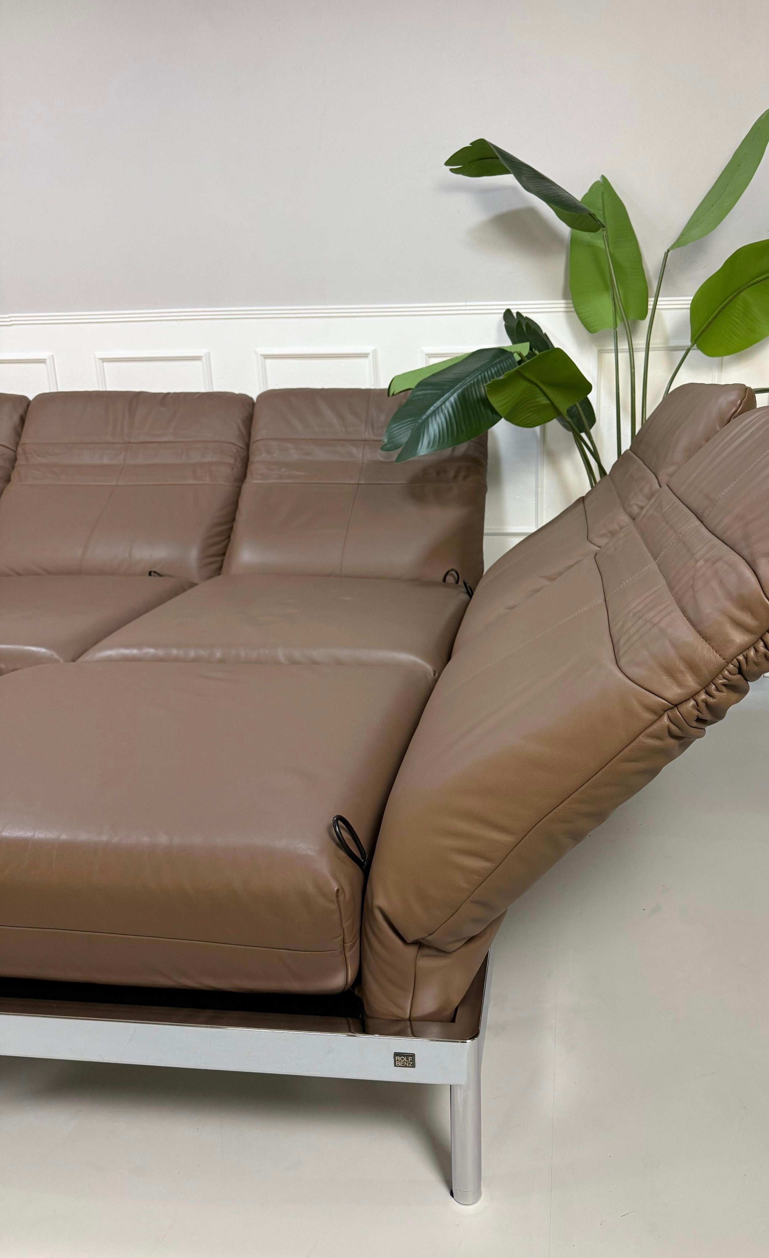 Gebrauchtes braunes Rolf Benz Plura Designer Leder Sofa mit Chromfüßen vor einer Wand, stilvoll und modern eingerichtet.