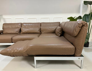 Gebrauchtes braunes Rolf Benz Plura Designer Leder Sofa mit Chromfüßen vor einer Wand, stilvoll und modern eingerichtet.