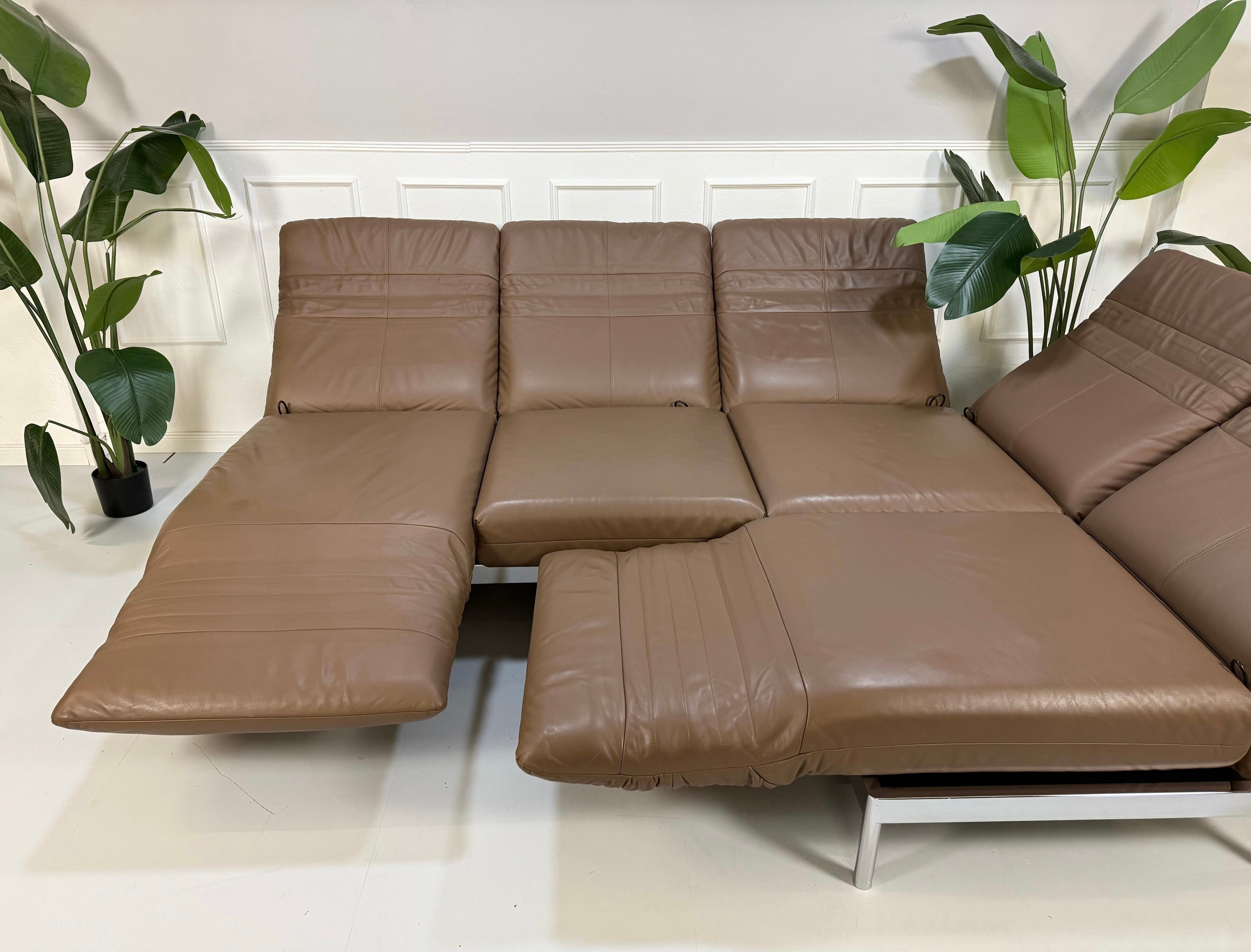 Gebrauchtes braunes Rolf Benz Plura Designer Leder Sofa mit Chromfüßen vor einer Wand, stilvoll und modern eingerichtet.