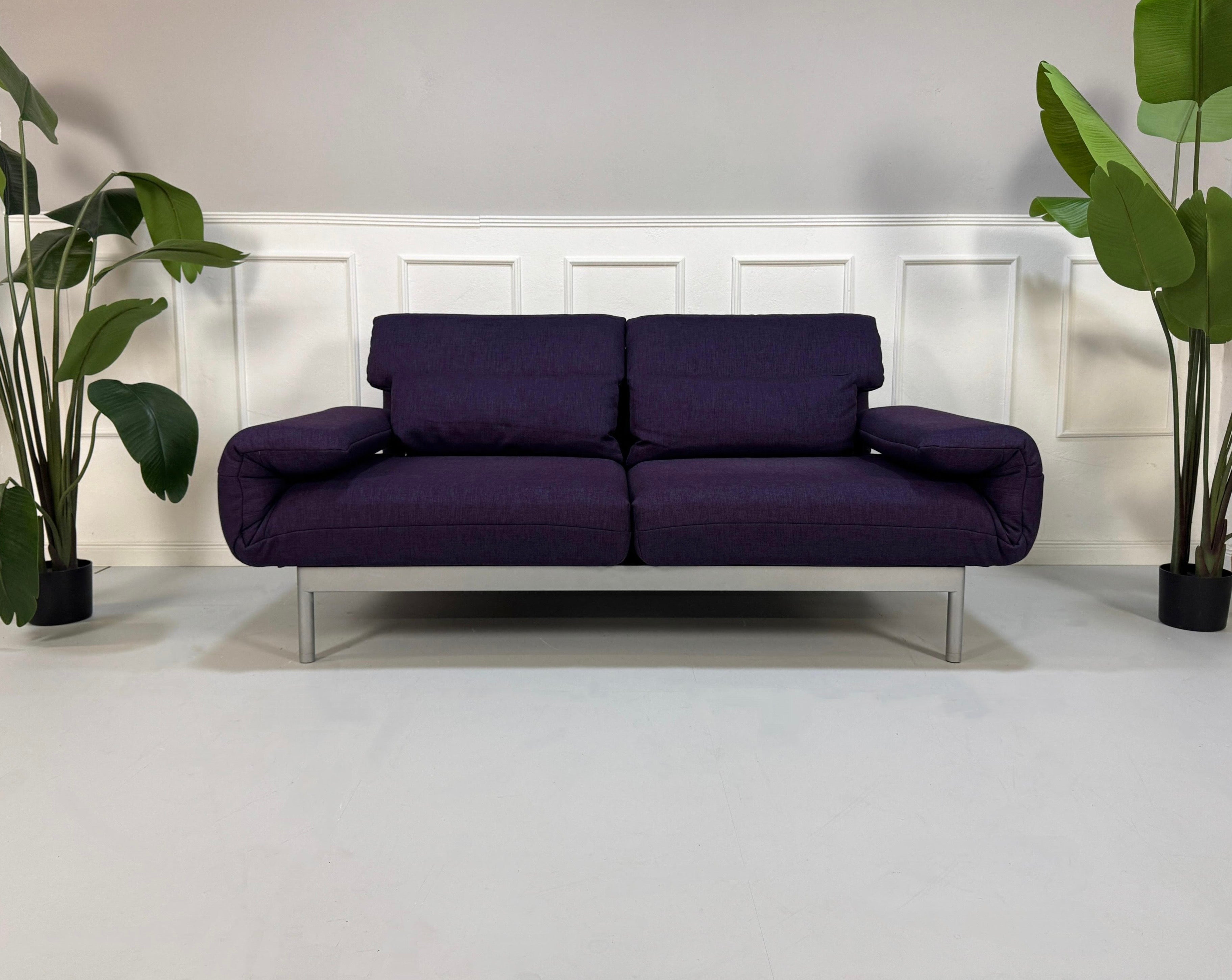 Gebrauchtes lila Rolf Benz Pura Designer Stoff Sofa vor einer Wand, stilvoll und modern eingerichtet.