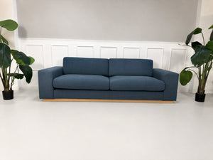Gebrauchtes blaues Bolia Sepia Designer Stoff Sofa vor einer Wand, stilvoll und modern eingerichtet.