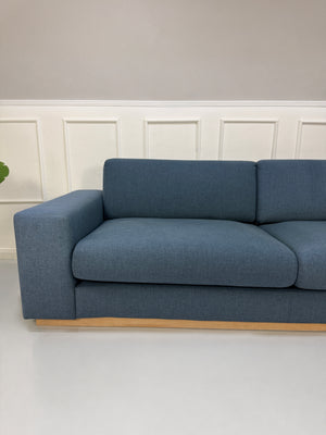 Gebrauchtes blaues Bolia Sepia Designer Stoff Sofa vor einer Wand, stilvoll und modern eingerichtet.