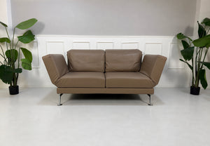 Gebrauchtes braunes Brühl Moule Medium Designer Leder Sofa vor einer Wand, stilvoll und modern eingerichtet.