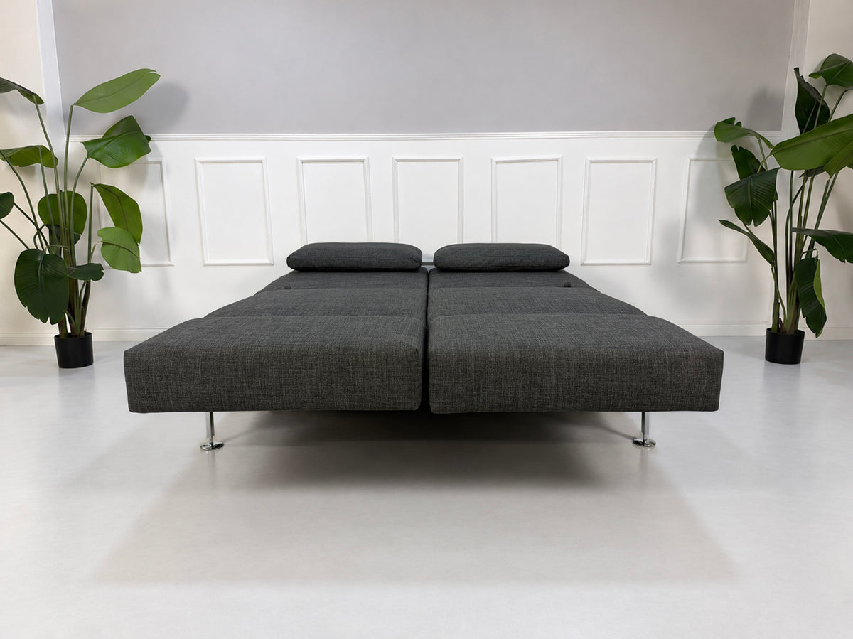 Gebrauchtes graues Brühl Moule Medium Designer Stoff Sofa vor einer Wand, stilvoll und modern eingerichtet.
