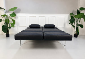 Gebrauchtes schwarzes Brühl Roro Soft Medium Designer Leder Sofa vor einer Wand, stilvoll und modern eingerichtet.