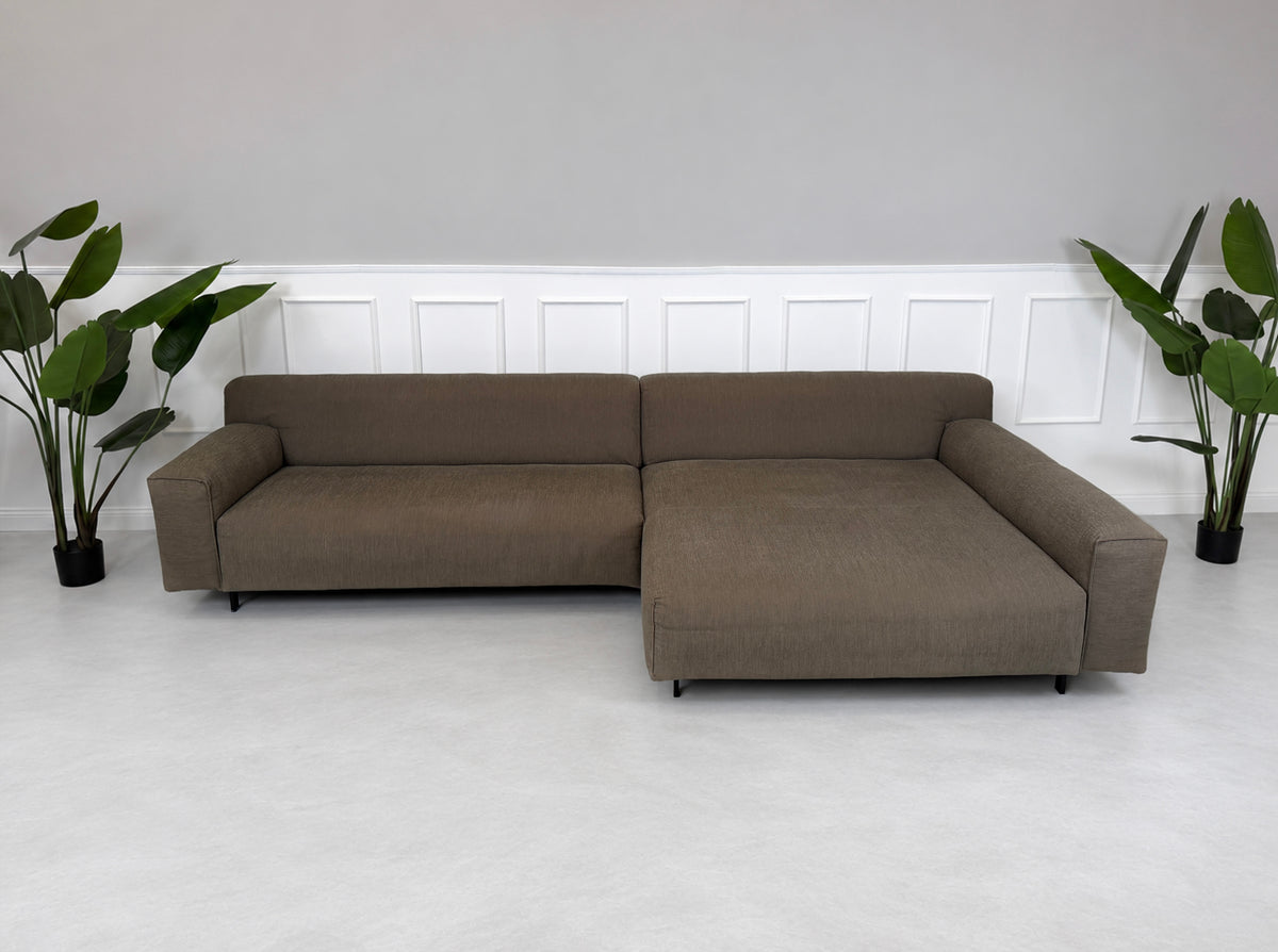 Gebrauchtes braunes Rolf Benz Grata Designer Stoff Ecksofa vor einer Wand, stilvoll und modern eingerichtet.
