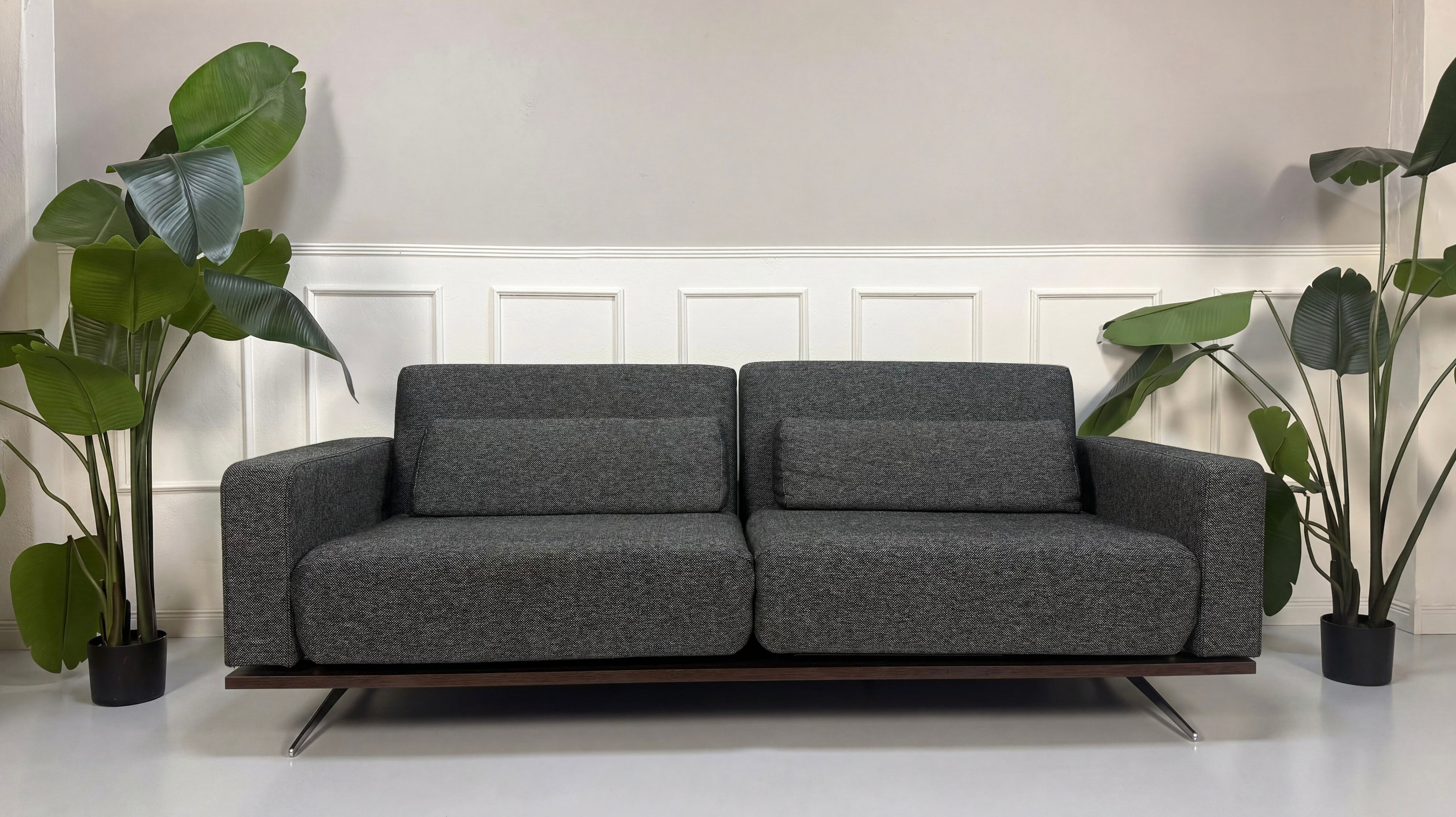 Gebrauchtes graues Studio Copenhagen Copperfield Designer Stoff Sofa vor einer Wand, stilvoll und modern eingerichtet.
