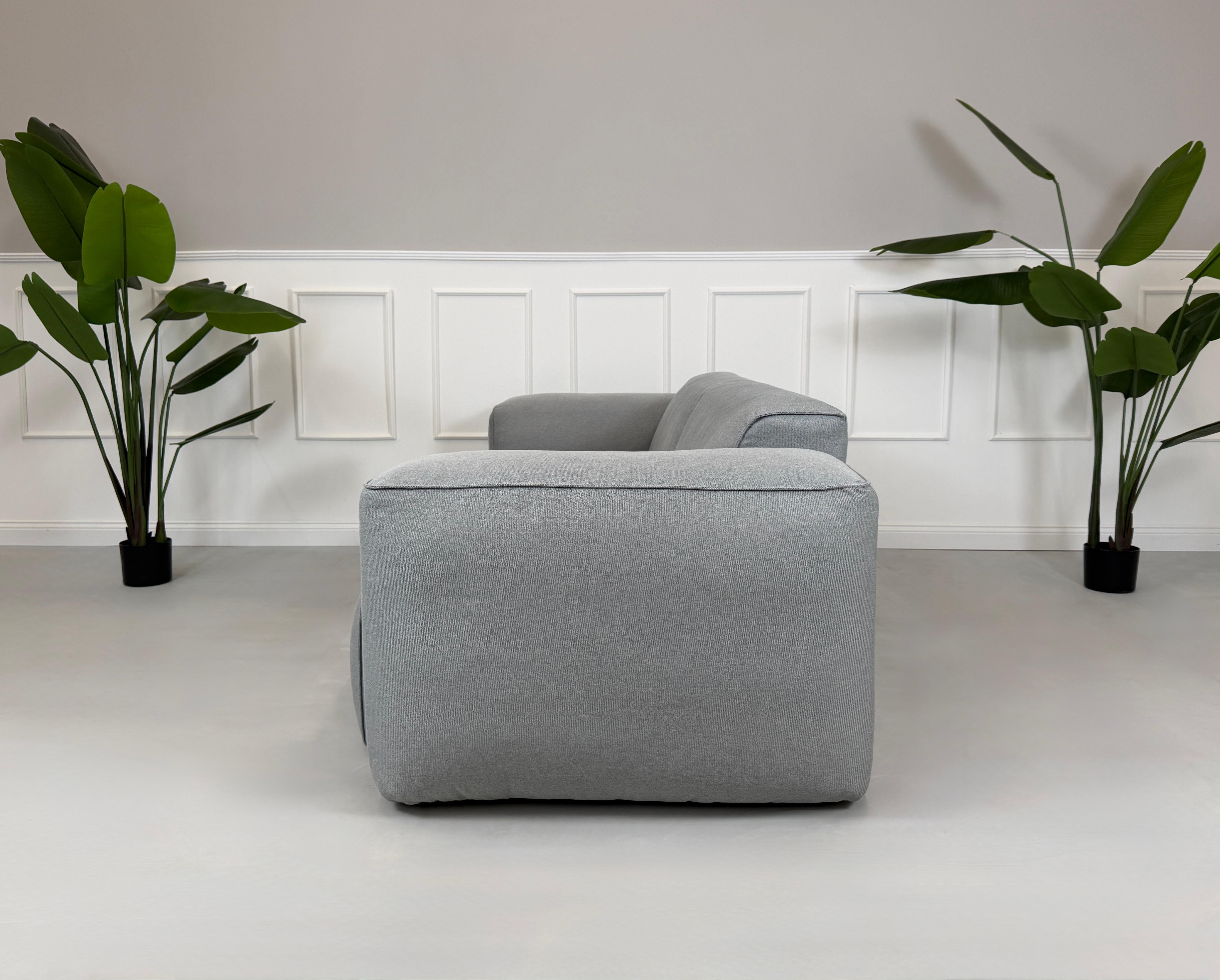 Gebrauchtes graues Stoff Sofa Studio Copenhagen Hudson vor einer modernen Wand.