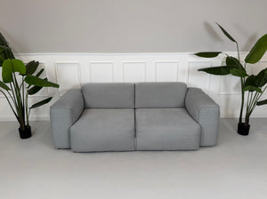 Gebrauchtes graues Stoff Sofa Studio Copenhagen Hudson vor einer modernen Wand.