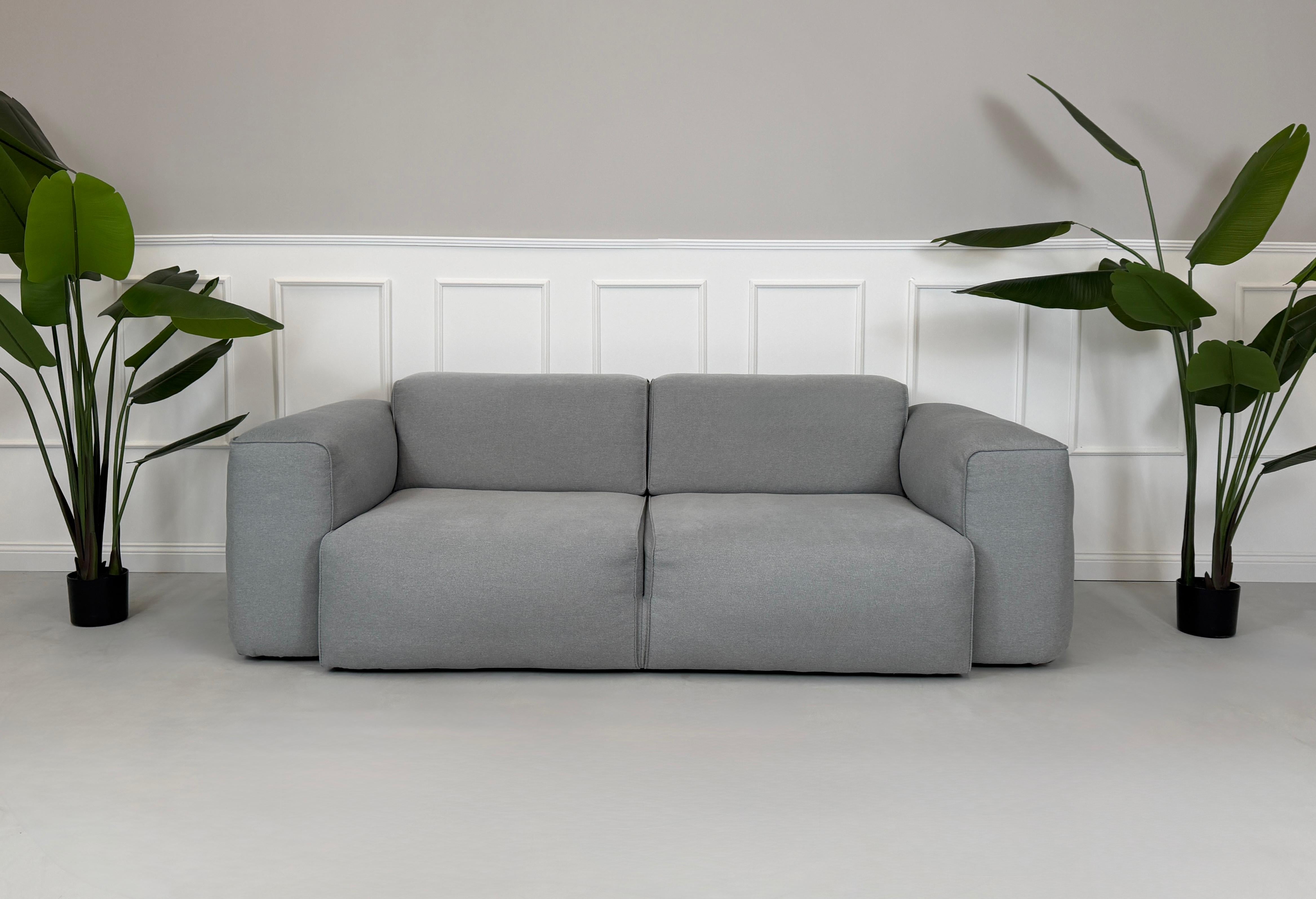 Gebrauchtes graues Stoff Sofa Studio Copenhagen Hudson vor einer modernen Wand.