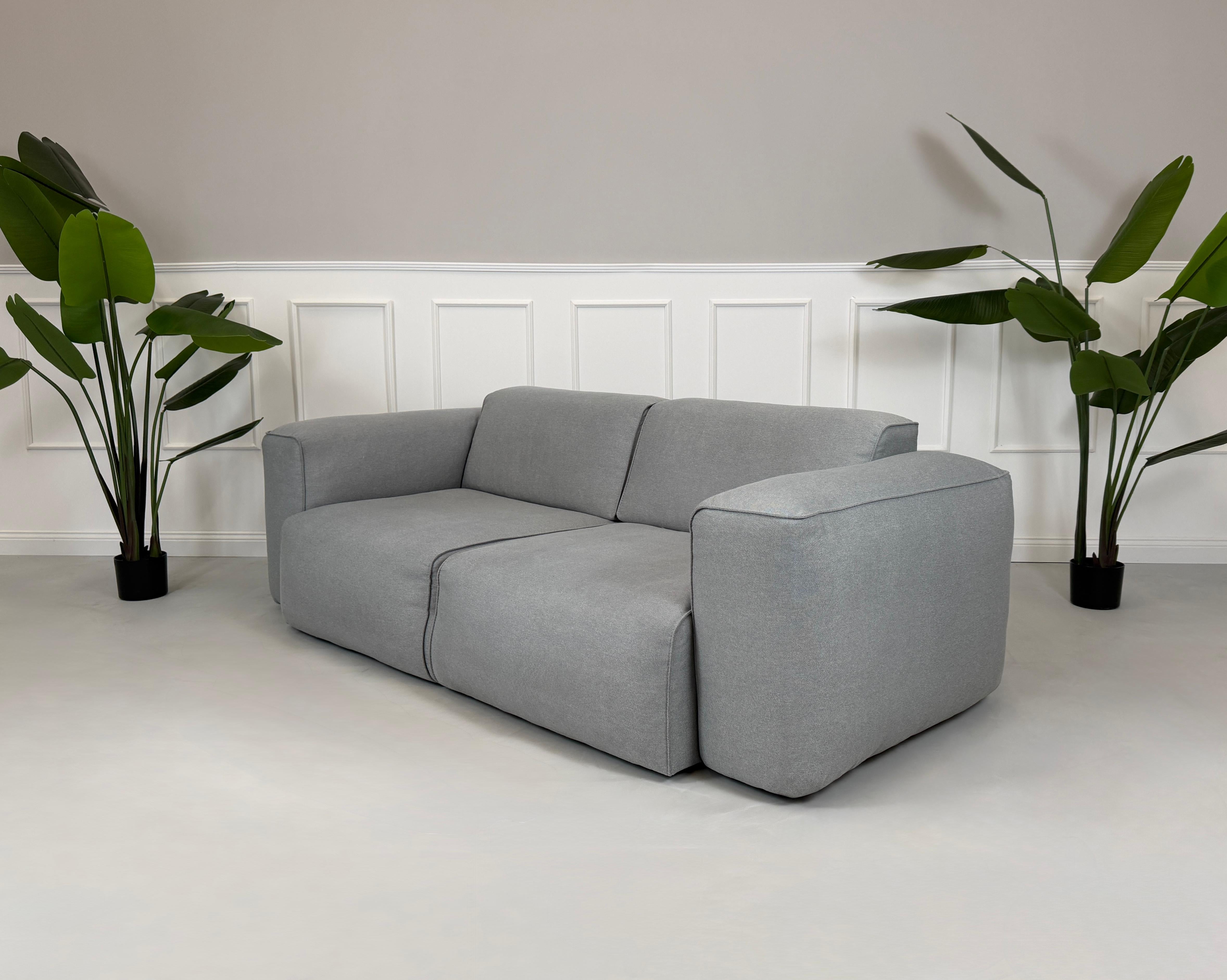 Gebrauchtes graues Stoff Sofa Studio Copenhagen Hudson vor einer modernen Wand.