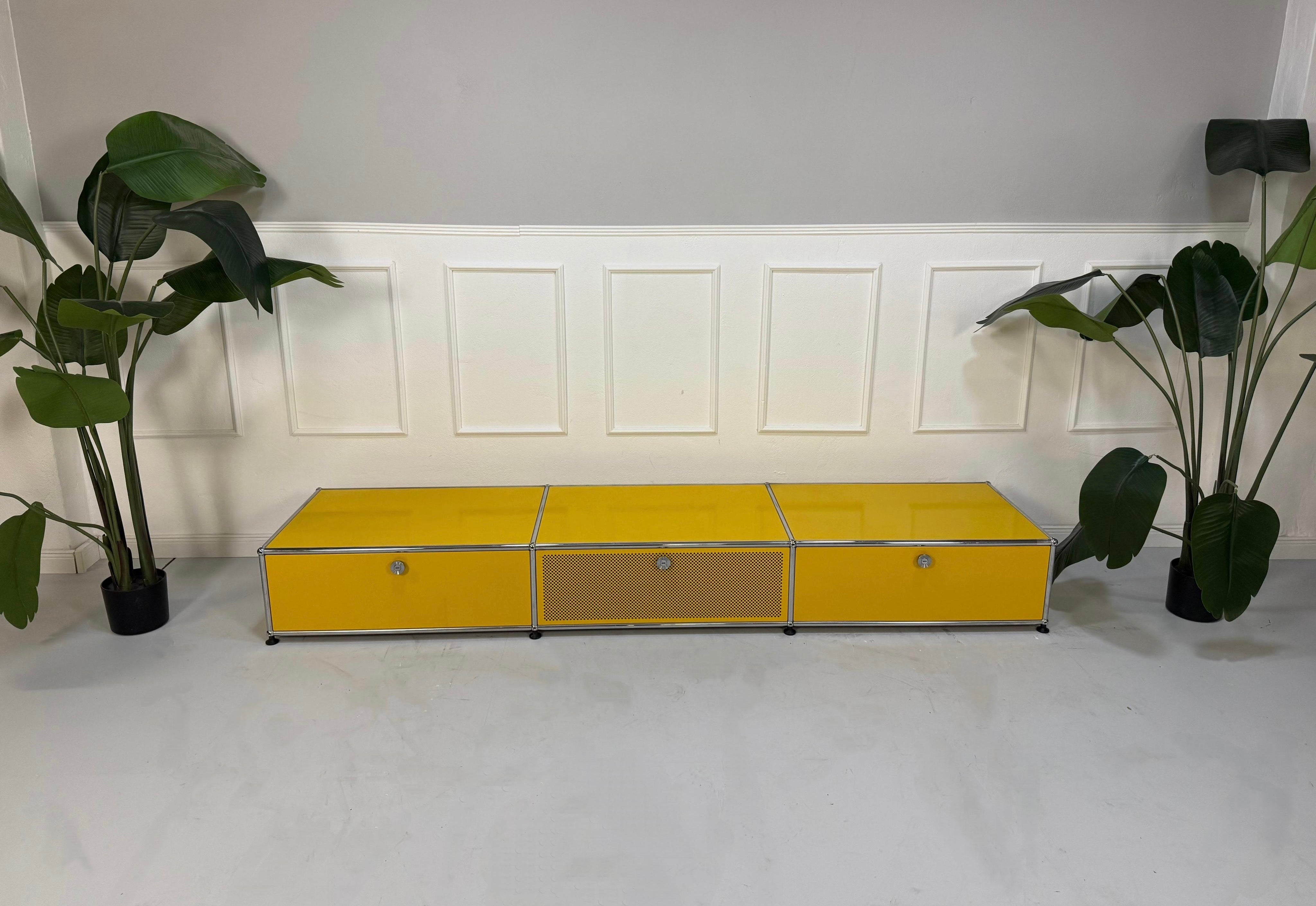 Gebrauchtes gelbes TV USM Haller Lowboard vor einer Wand, stilvoll und modern eingerichtet.