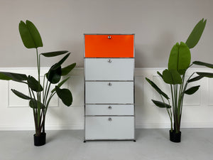Gebrauchtes USM Haller Designer Regal in den Farben Orange und Grau vor einer Wand, stilvoll und modern eingerichtet.
