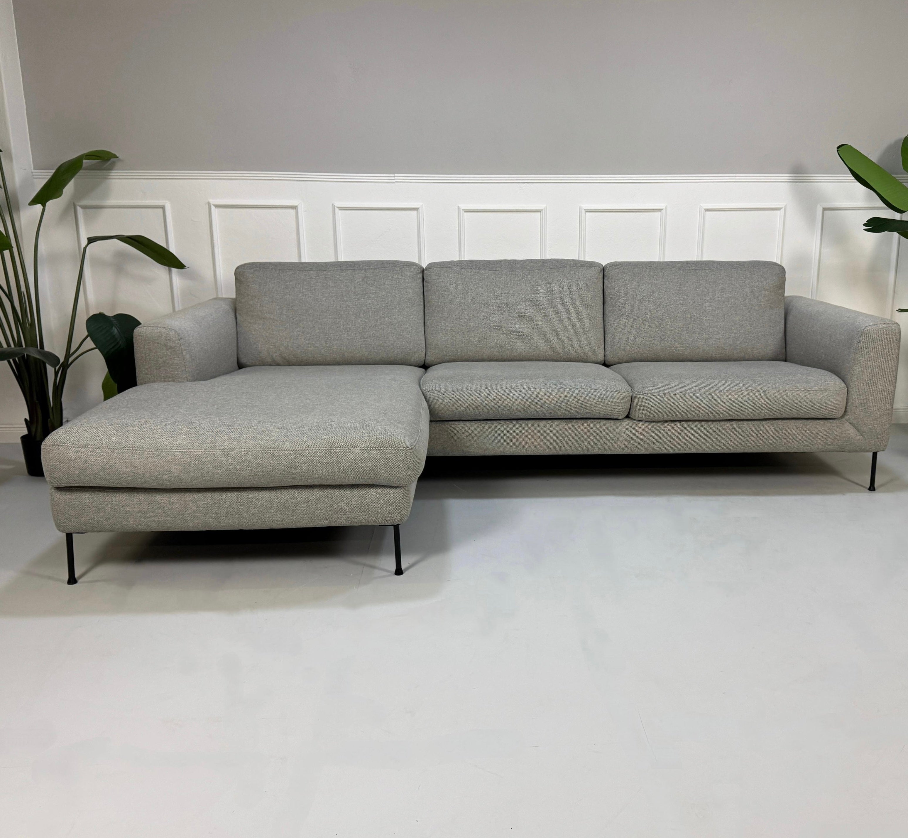 Gebrauchtes graues Westwing Cucita Designer Stoff Sofa vor einer Wand, stilvoll und modern eingerichtet.