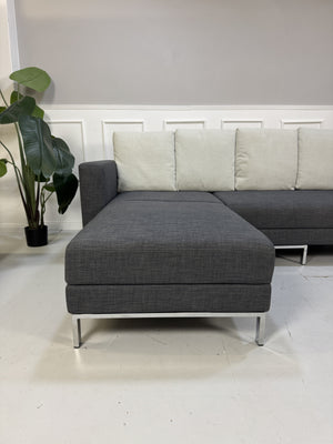 Gebrauchtes graues Brühl Fourtwo Designer Stoff Ecksofa vor einer Wand, stilvoll und modern eingerichtet.