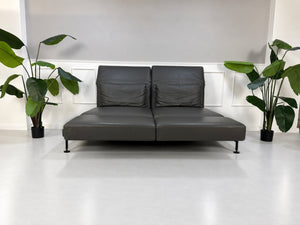 Gebrauchtes braunes Brühl Moule Large Designer Leder Sofa vor einer Wand, stilvoll und modern eingerichtet.