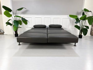 Gebrauchtes braunes Brühl Moule Large Designer Leder Sofa vor einer Wand, stilvoll und modern eingerichtet.